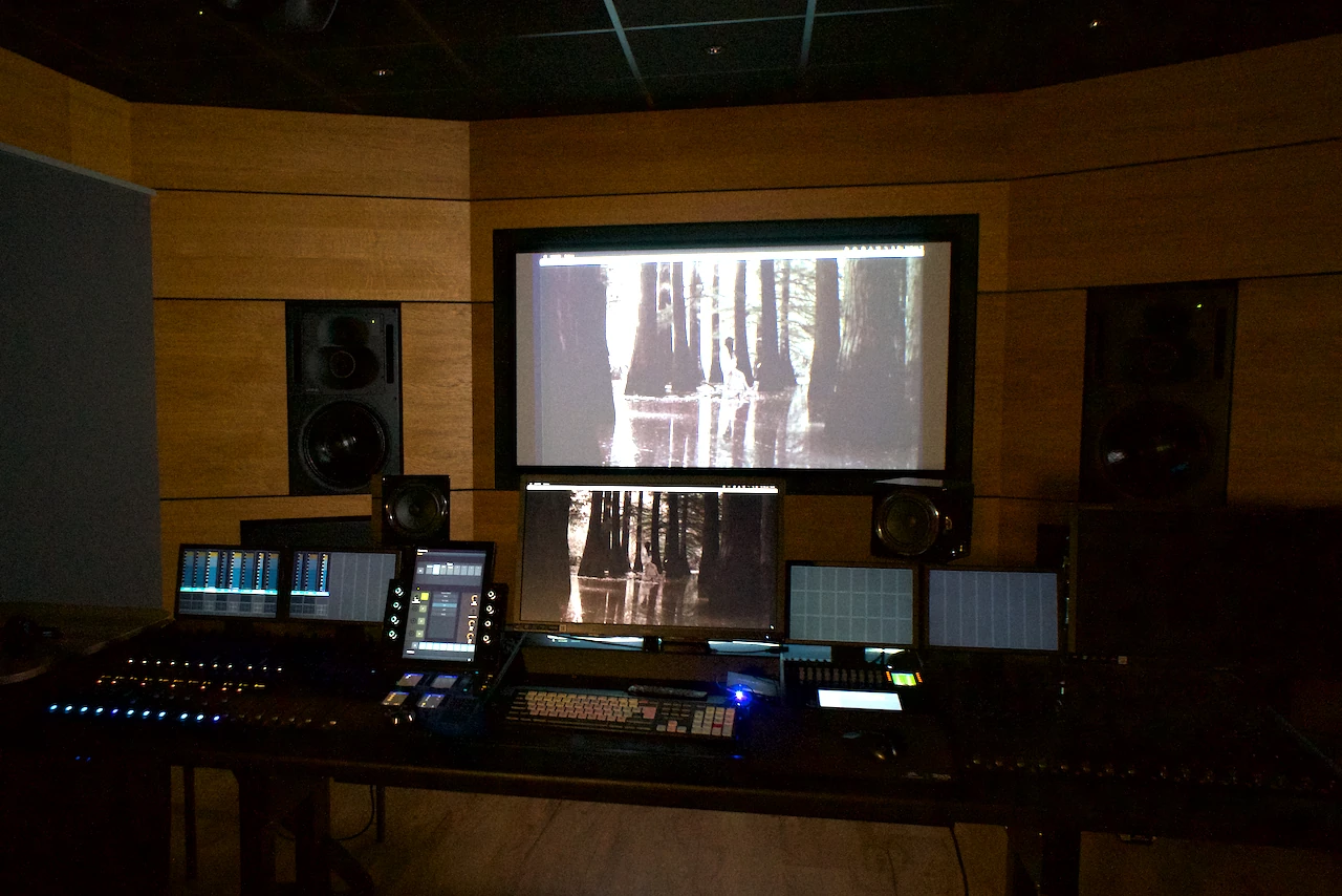 In a dim sound studio, we look at sound studio mixing desk and a screen with a black and white film clip.