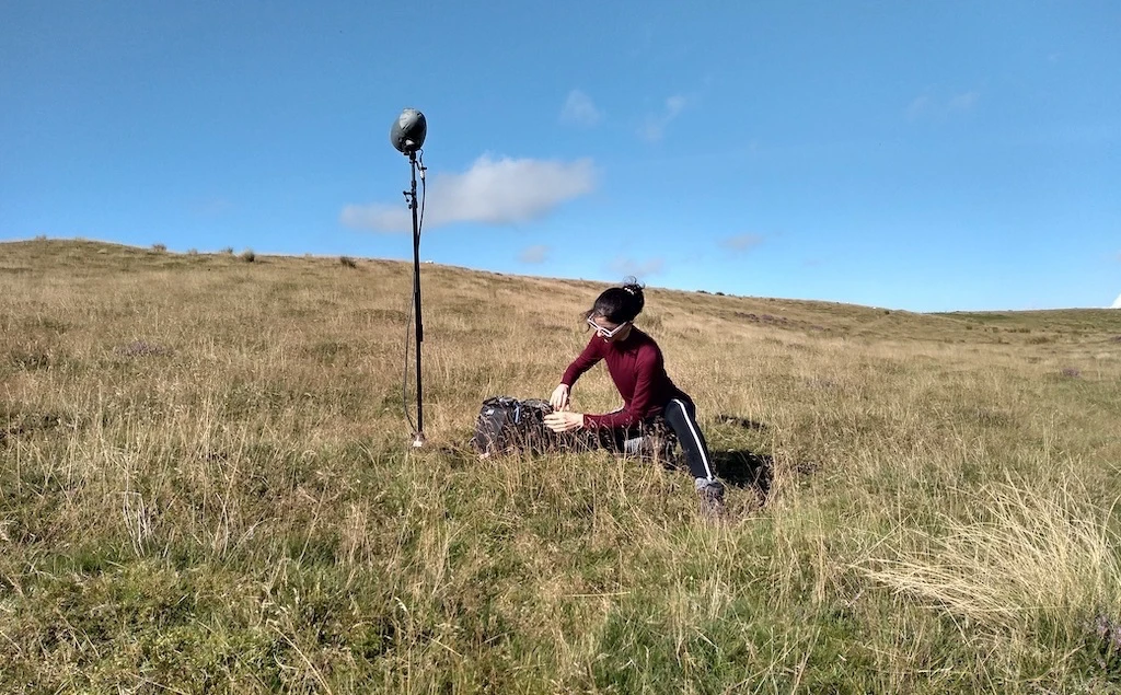 Mariana sitting on hill with microphones.