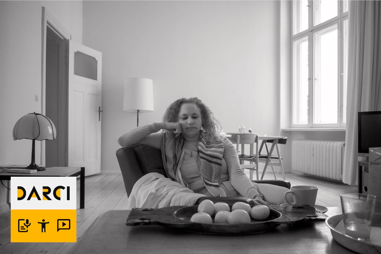 ‘A greyscale photo of Maria sitting in room.’