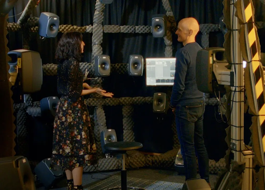 Mariana and Gavin standing in a spacious room equipped with large speakers.