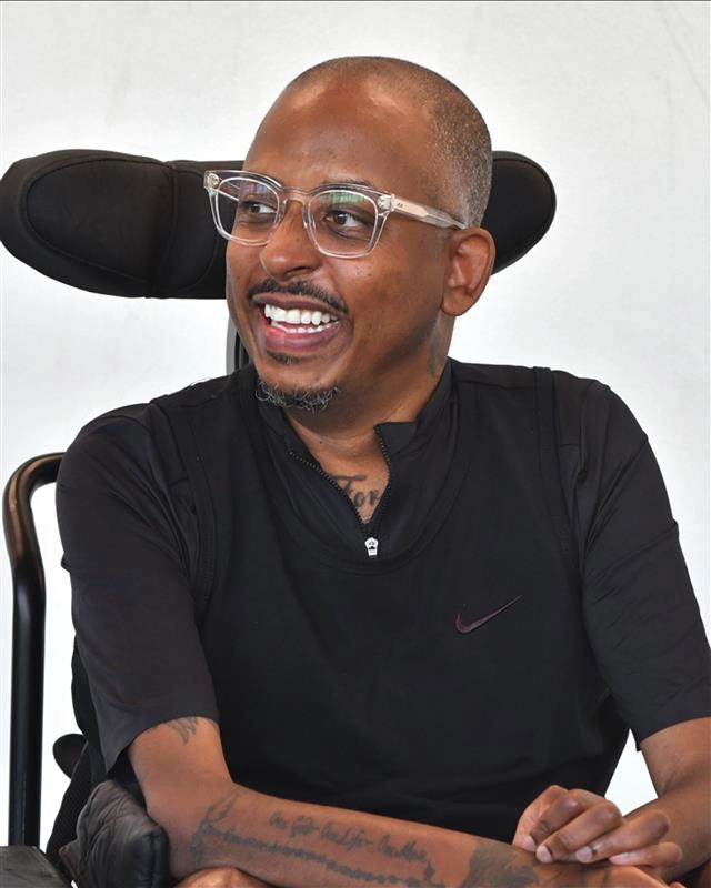 Samuel sits in his chair smiling.