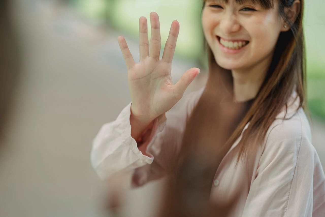 A female person smiling and waving with her righ hand.